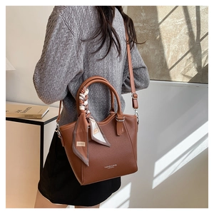 Gros plan du sac seau en cuir litchi marron avec foulard décoratif et lettrage doré