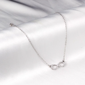 Infinity pendant necklace with white crystals on white silk background
