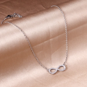 Elegant silver infinity necklace with sparkling diamonds on champagne silk background