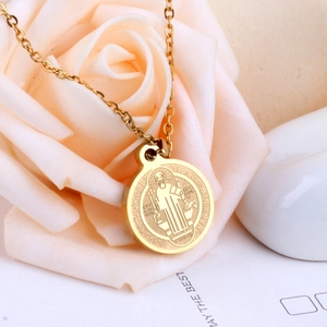 Close-up of a gold Saint Benedict medal necklace nestled in soft rose petals