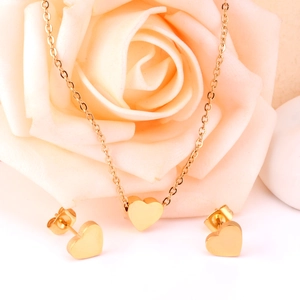 Close-up of golden heart pendant necklace and matching stud earrings on rose background