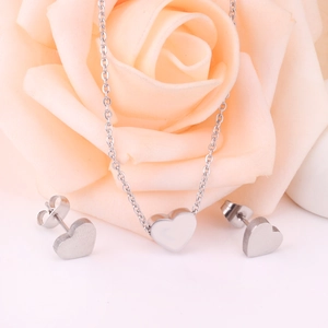 Close-up of heart necklace and earrings set with rose petals on a soft background