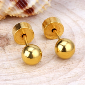 Macro shot of minimalist gold round stud earrings on a natural wood surface
