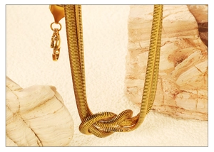 Détail macro du collier chaîne serpent plaqué or avec un nœud central élégant