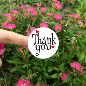 Detail of round white 'Thank You' sticker with heart patterns held in hand outdoors