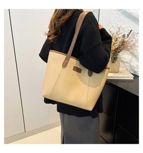 Detailed side view of a large cream faux leather tote bag worn by a model in a room