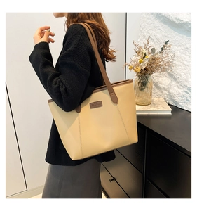 Detail view of large beige tote bag with brown trim and embossed fashion logo leather tag
