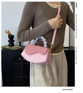 Détail du sac à bandoulière rose avec poignée en perles de marbre porté par un mannequin