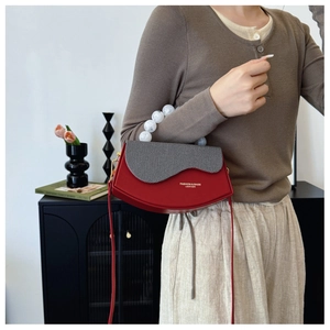 Détail d'un sac en cuir rouge avec rabat gris et poignée élégante en perles blanches