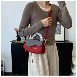 Détail du sac rouge semi-circulaire avec poignée en perles et rabat gris texturé