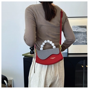 Détail du sac croissant en cuir rouge avec rabat rayé et poignée en perles blanches