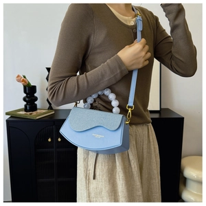 Détail du sac demi-lune bleu clair avec rabat tissé et poignée en perles marbrées