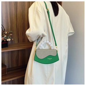 Détail du sac bandoulière vert avec rabat texturé et grande poignée en perles sur manteau