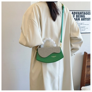 Détail du sac boîte en cuir vert avec rabat en tissu gris et poignée en perles translucides