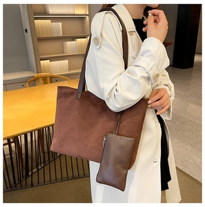 Brown suede tote bag with matching pouch shown on a model in a warm interior setting