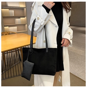 Detail of black suede tote bag with matching pouch on model in a modern office