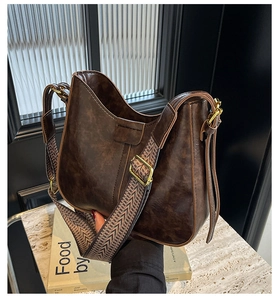 Détail du sac seau en cuir marron foncé avec bandoulière jacquard et boucles dorées