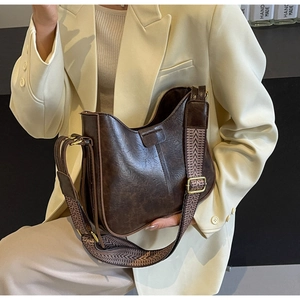 Détail du sac seau marron vintage avec une large bandoulière tissée et boucle dorée