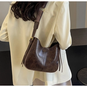 Détail d'un sac seau vintage en cuir marron avec large bandoulière tissée géométrique