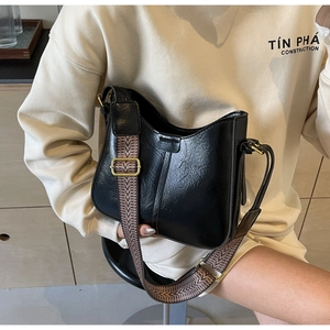 Détail du sac demi-lune noir brillant avec boucle dorée et bandoulière tissée en zigzag