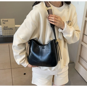 Détail du sac seau noir en demi-lune avec bandoulière jacquard et boucles dorées