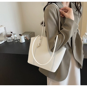 Model wearing a white bucket tote bag with lychee grain texture in a modern cafe setting