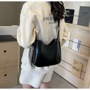 Détail du sac seau en cuir noir brillant avec large bandoulière porté par un modèle