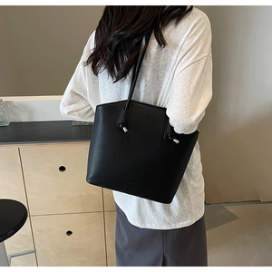 Detailed view of black lychee grain leather tote bag with gold metal hardware on model
