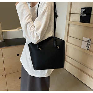 Detail of minimalist black pebbled leather tote bag with thin shoulder straps on a model