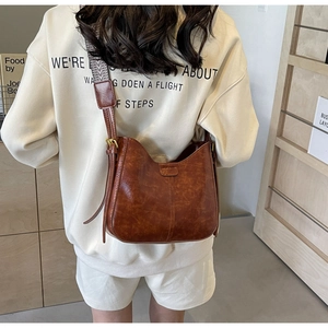 Détail d'un sac seau vintage en cuir marron avec large bandoulière sur modèle