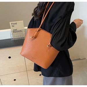 Close-up of brown pebble leather tote bag featuring knotted handles and metallic hardware