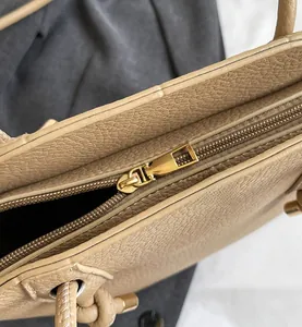 Close-up of golden zipper and lychee pattern leather on beige bucket tote bag
