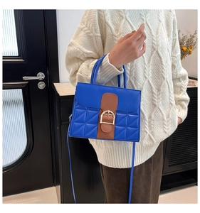 Détail d'un sac en cuir matelassé bleu avec boucle dorée sur un pull en maille beige