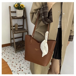 Brown leather tote bag with white silk scarf detail shown in a cozy interior setting