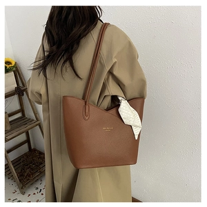 Detail of a brown lychee pattern crossbody bag with decorative silk scarf and gold logo