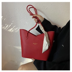Detail of red litchi texture leather tote bag featuring a decorative silk scarf on the handle
