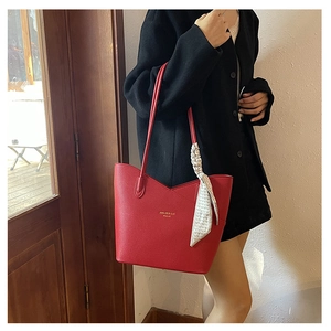 Detail of red pebbled leather tote bag featuring a stylish silk scarf and golden logo