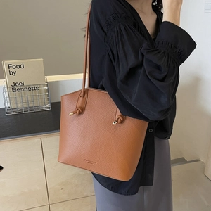 Brown lychee leather bucket tote bag with knotted handles worn by a female model