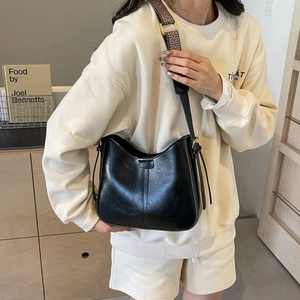 Sac seau rétro noir en cuir texturé avec large bandoulière géométrique sur modèle