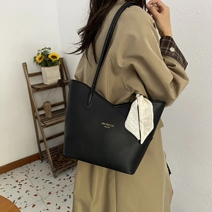 Black pebbled leather tote bag with silk scarf accessory worn over a beige coat