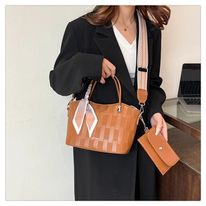 Dettaglio borsa shopper marrone intrecciata con foulard di seta e tracolla geometrica