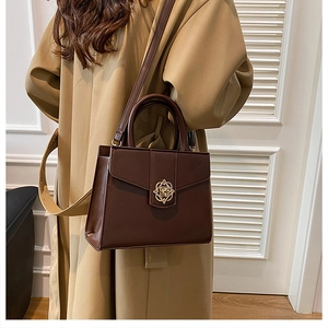 Sac à main marron foncé avec fermoir floral doré porté par un mannequin en trench