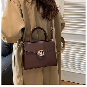 Détail d'un sac à main en cuir marron foncé avec fermoir fleur dorée et manteau kaki