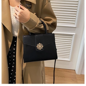 Détail d'un sac à main noir avec boucle florale dorée sur un trench-coat de couleur kaki