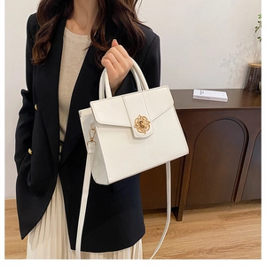 Gros plan d'un sac blanc avec boucle florale dorée et poignée fixe pour femme