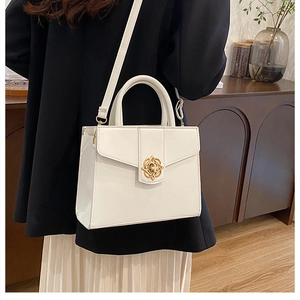 Gros plan sur le sac blanc avec fermoir floral doré porté par un mannequin en intérieur