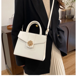 Détail du sac à main blanc avec fermoir trèfle doré porté sur une veste noire