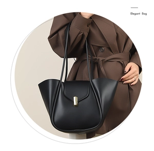 Détail du sac cabas noir avec plis incurvés et boucle dorée sur un manteau marron