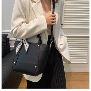 Détail du sac seau noir en cuir grainé avec une écharpe en soie décorative sur la poignée
