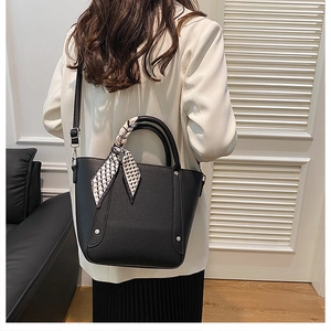 Détail d'un sac seau noir en cuir texturé avec foulard géométrique décoratif sur l'anse